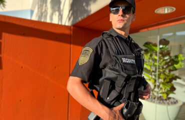 Professional security guard in tactical uniform standing alert outside a commercial building, demonstrating proactive security presence and risk prevention