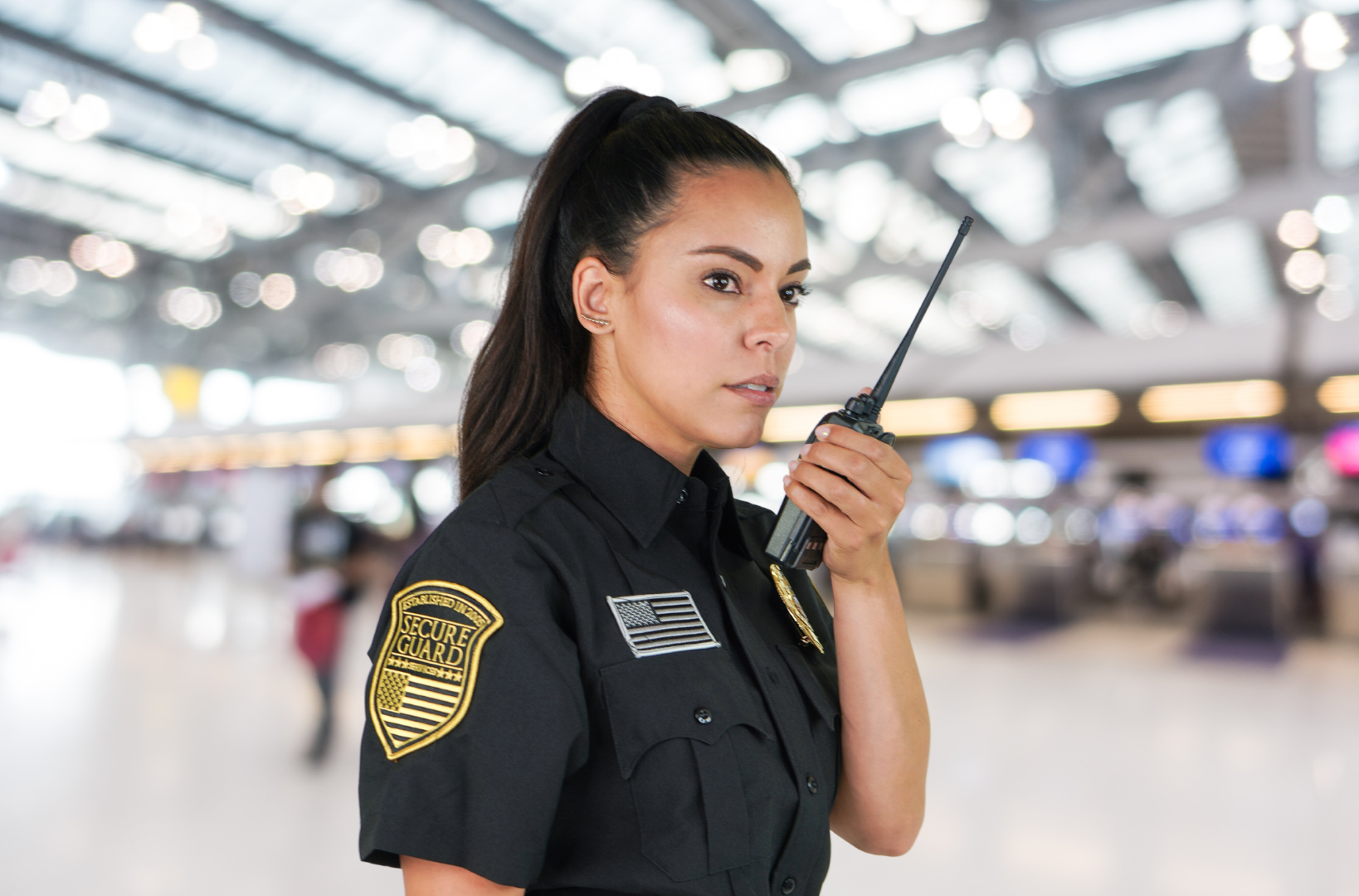 Security guard using a two-way radio inside a busy facility, coordinating emergency response and evacuation procedures
